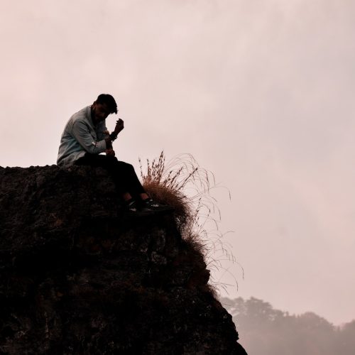 a man sitting on top of a rock next to a grass covered hillside